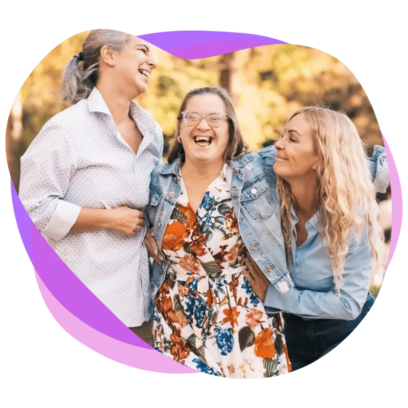 Two female support workers embracing their female friend with a disability