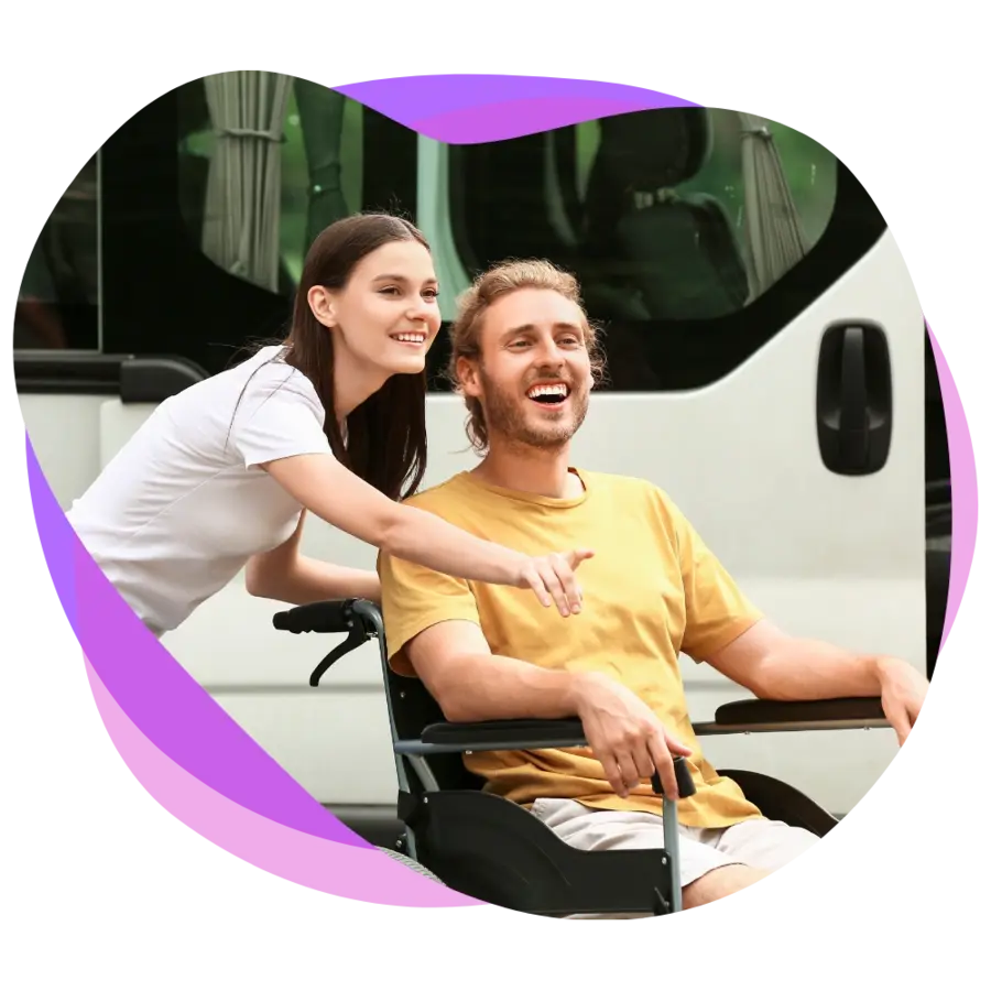 Young adult male participant in a wheelchair smiling as he is being assisted by his female support worker