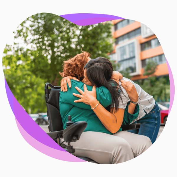 Female support worker hugging female participant in wheelchair